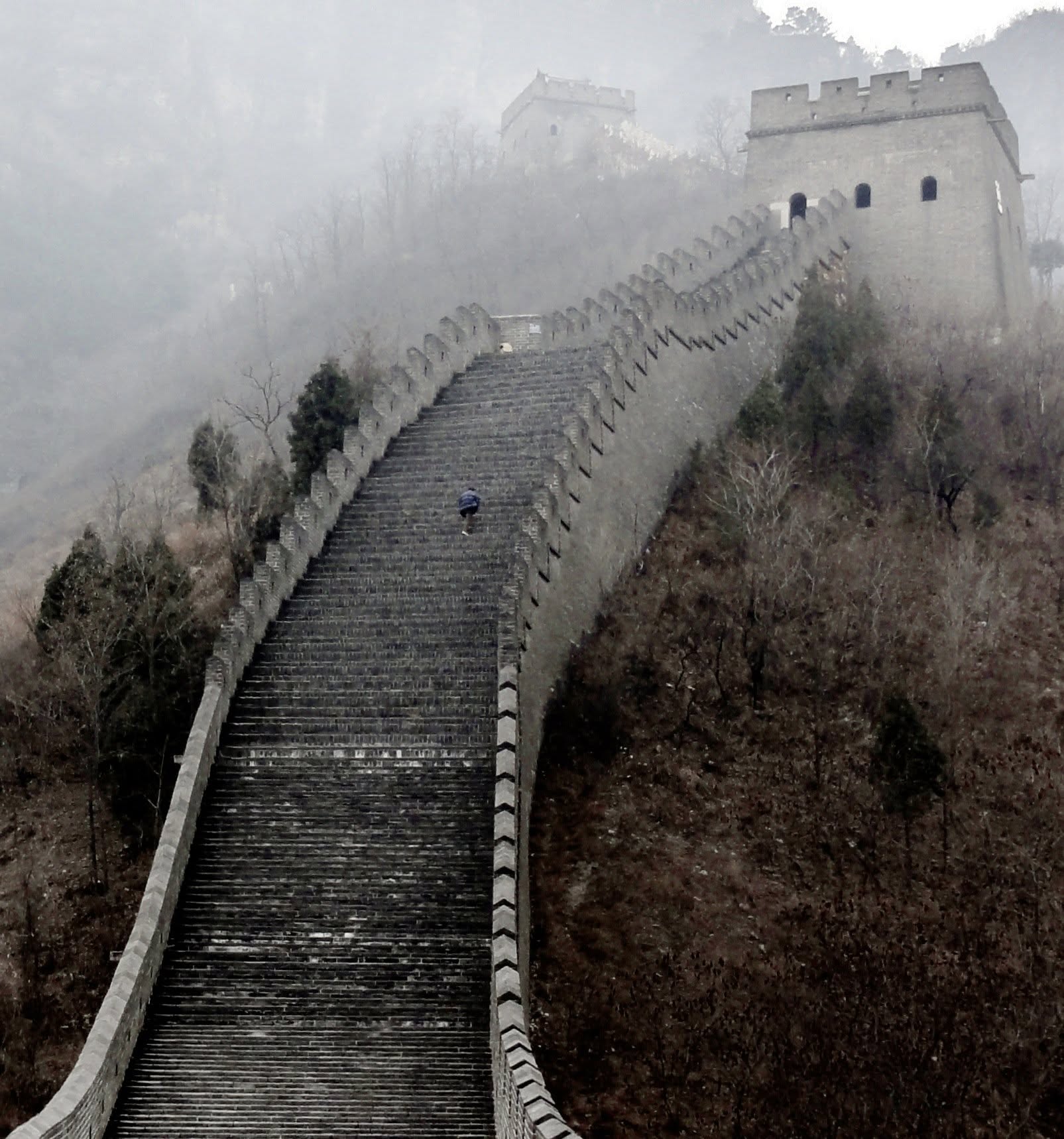 The Great Wall of China in mist, a lone figure climbing steep stone steps