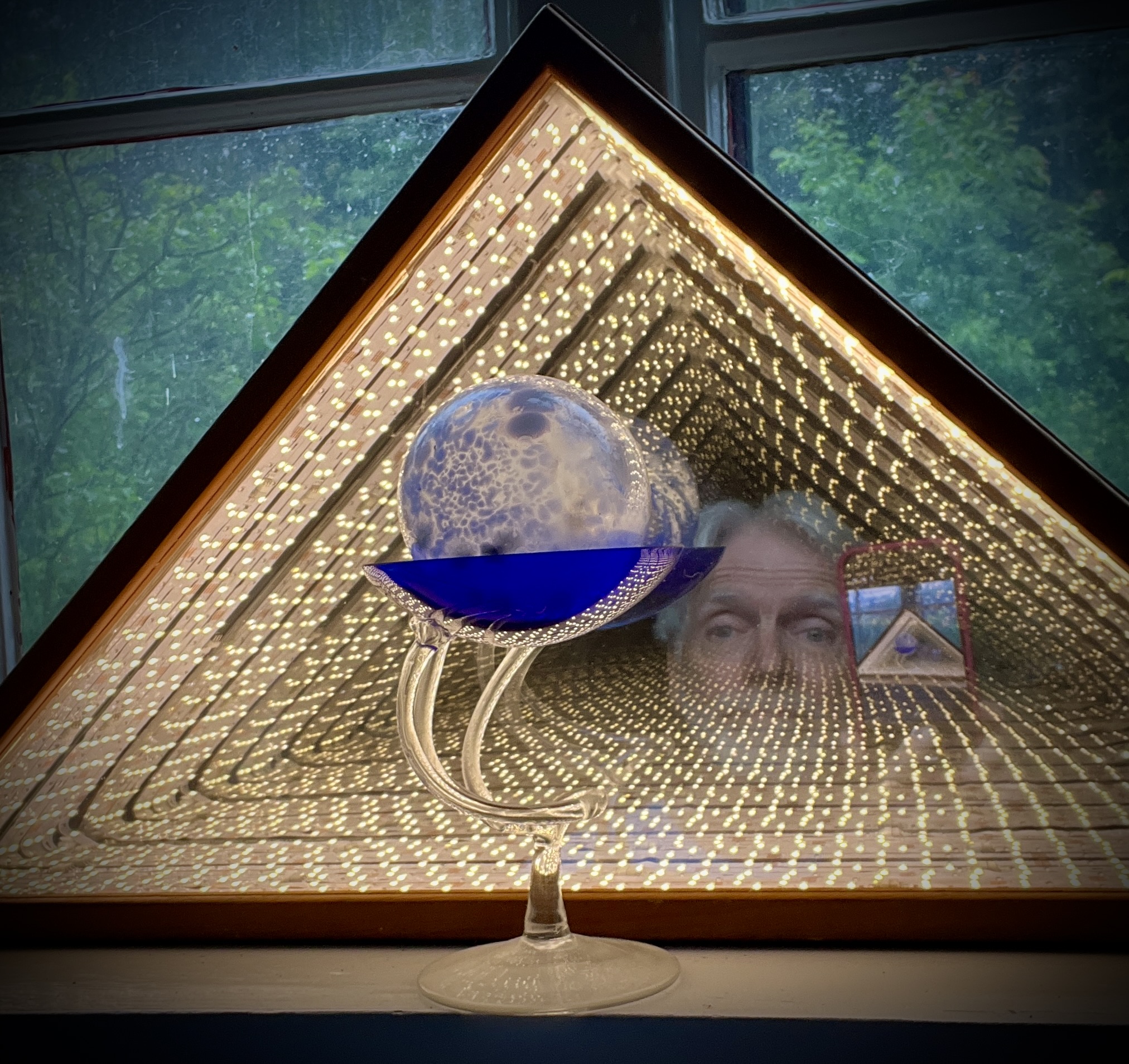 Crystal ball reflecting Dan Lloyd against a triangular light installation